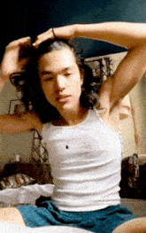 a man with long hair is wearing a white tank top and blue shorts
