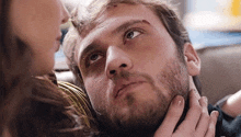 a man with a beard is laying on a couch with a woman kissing his neck .