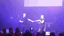 two men shaking hands on a stage with a crowd watching