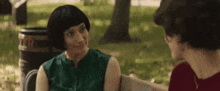two women are sitting on a park bench talking to each other . one of the women is wearing a wig .