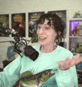 a woman wearing glasses and a sweater with a fish on it is smiling in front of a microphone .