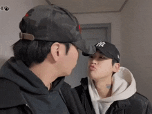 a man wearing a ny hat kisses another man