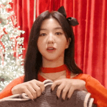 a woman wearing a red choker is holding a sweater in front of a christmas tree .
