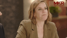 a woman sitting at a table in front of a sign that says mkr
