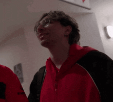 a man wearing glasses and a red jacket is smiling and looking up