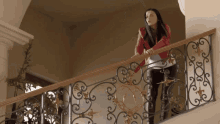a woman in a red jacket stands on a balcony with a wrought iron railing