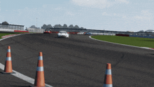 a white car is driving down a race track with orange and white cones