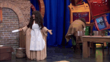 a woman in a white apron is standing on a stage in front of a blue curtain