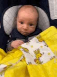 a baby in a car seat with a yellow blanket