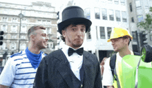 a man wearing a top hat and a bow tie stands next to a man wearing a hard hat
