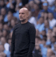 a bald man in a black shirt stands in front of a crowd of people