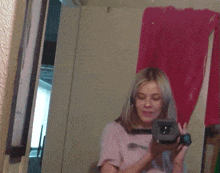 a woman in a pink shirt is holding a video camera in front of a mirror