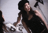 a woman in a black tank top is getting her hair done by another woman in a black beret