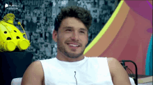 a man wearing a white tank top is smiling in front of a playplus logo