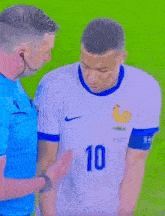 a soccer player wearing a white shirt with the number 10 on it is talking to a referee .