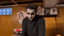 a man with a clown face painted on his face is standing in a room