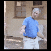 a man in a blue shirt is standing in front of a window with his arms outstretched