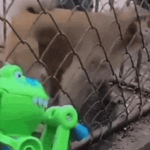 a green toy is standing next to a fence