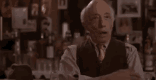 a man in a suit and tie is sitting at a table in a bar talking to someone .