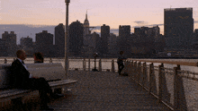 a man sits on a bench with a view of the city skyline behind him