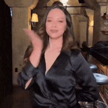 a woman wearing a black satin shirt is dancing in a room .