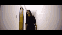 a woman wearing glasses and a black shirt is walking down a hallway .