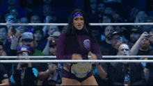 a woman in a purple outfit is standing in a wrestling ring holding a championship belt .