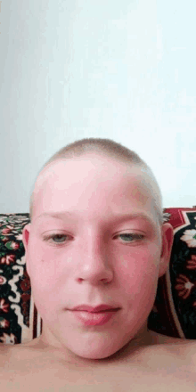 a young boy with a shaved head is laying on a couch looking at the camera