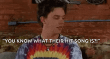 a man in a tie dye shirt is sitting on a couch and talking to another man .