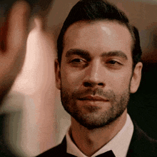 a man with a beard is wearing a black suit and bow tie