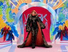 a woman in a long leopard print coat is standing in front of a neon sign that says work