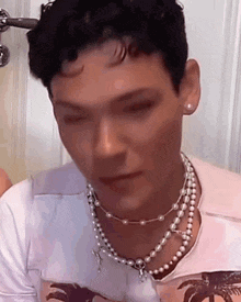 a man wearing a pearl necklace and earring is looking down .