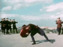a group of soldiers are standing around a man in a red shirt who is on his knees