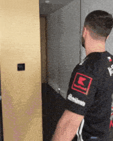 a man in a black shirt with a red k on the sleeve is standing in a hallway