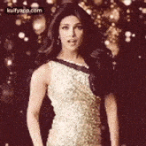 a woman in a gold sequined dress is standing in front of a blurred background .