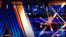 a man performing aerial acrobatics on a stage with the nbc logo in the background