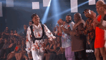 a group of people are applauding a man in a floral shirt with the bet logo in the background