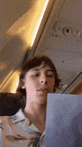a young man in a hawaiian shirt is reading a book on an airplane