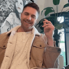 a man wearing a tan jacket and a white shirt is smiling with his eyes closed