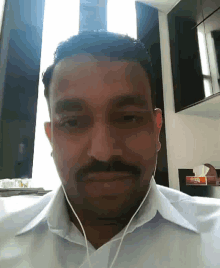 a man with a mustache wearing a white shirt and ear buds