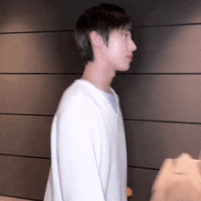 a young man is standing in front of a wall wearing a white sweater .