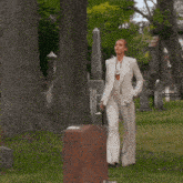 a woman in a white suit walks through a cemetery holding a cane