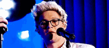 a man is singing into a microphone while wearing glasses .