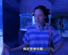 a woman wearing a blue and white striped shirt is standing in front of an aquarium