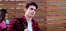 a young man wearing a plaid shirt and carrying a backpack