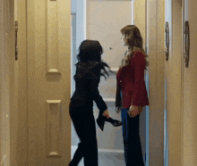 two women are standing in a hallway and one is holding a pair of high heels
