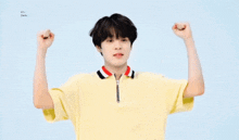 a young boy in a yellow shirt is making a funny face with his arms in the air .