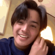 a young man in a blue shirt is smiling while talking on a phone .