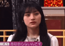 a woman with long black hair is sitting in front of a microphone and making a funny face .