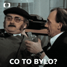a man in a beret holds a glass while another man says co to bylo